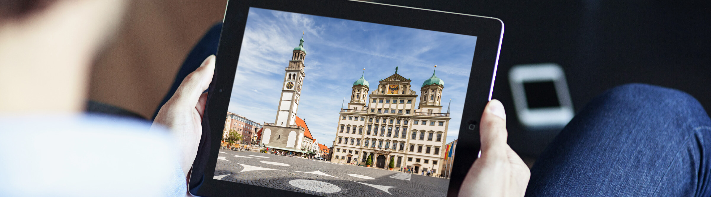 Header Bild von Augsburg auf einem Tablet, das ein Mann in der Hand hält