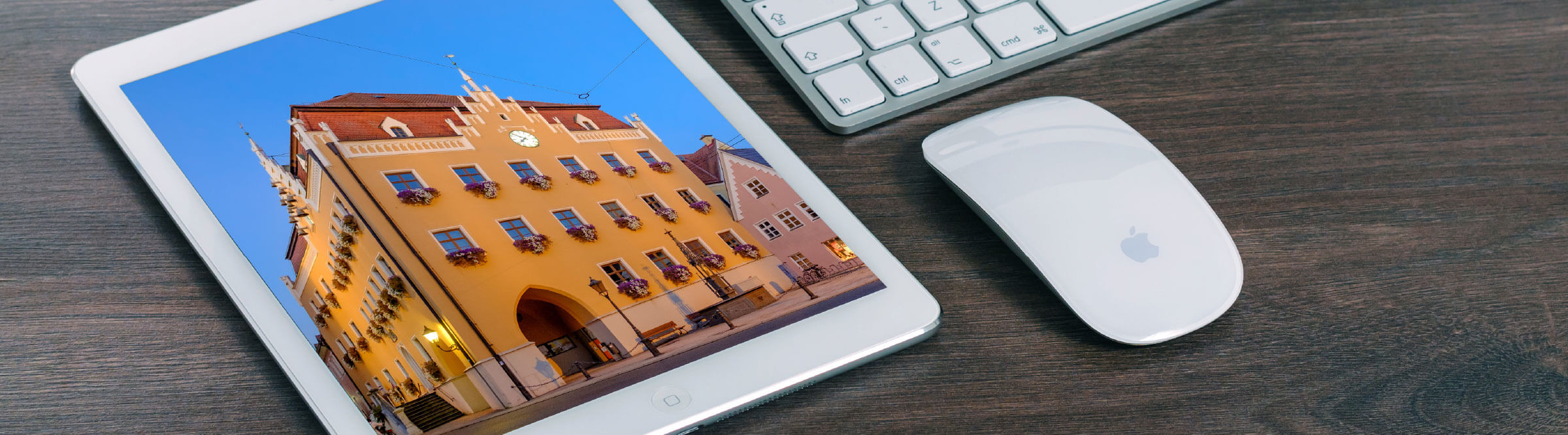 Header Bild von Ingolstadt auf einem Tablet, das auf einem Holzschreibtisch neben einer Tastatur und neben einer Maus liegt