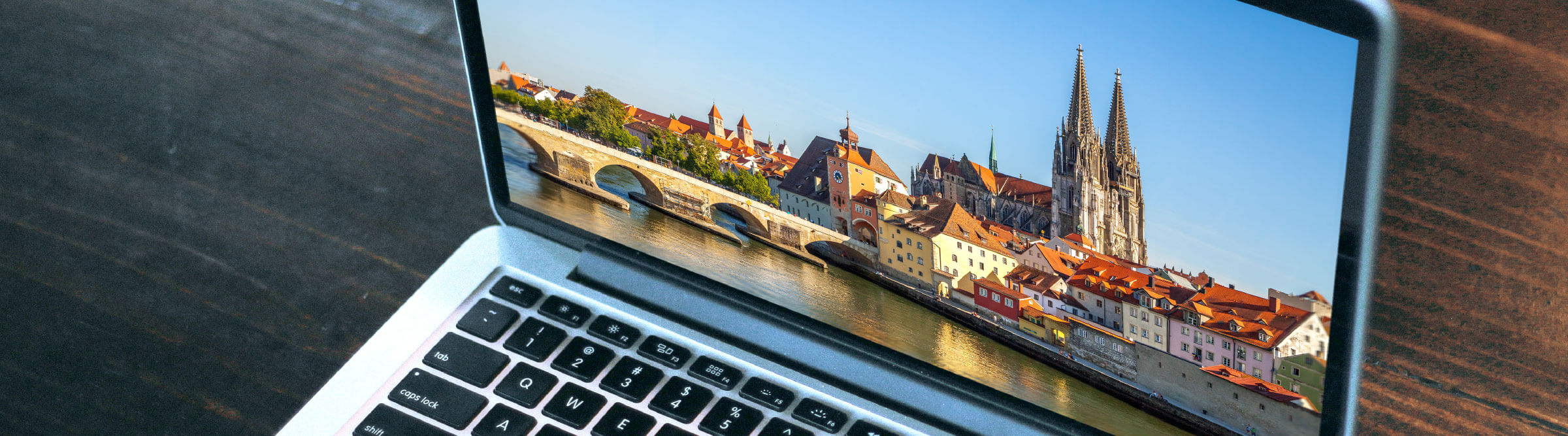 Header Bild von Regensburg auf einem Laptop, der auf einem dunklen Schreibtisch steht